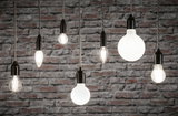 Verschiedene Filament-Glühbirnen mit schwarzer Fassung vor grauer Backsteinwand, Beleuchtung und Lampen.