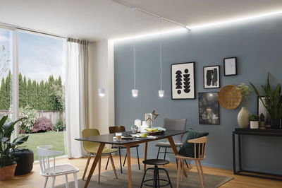 Salle à manger moderne avec table noire, chaises variées et éclairage LED sur rail blanc au plafond