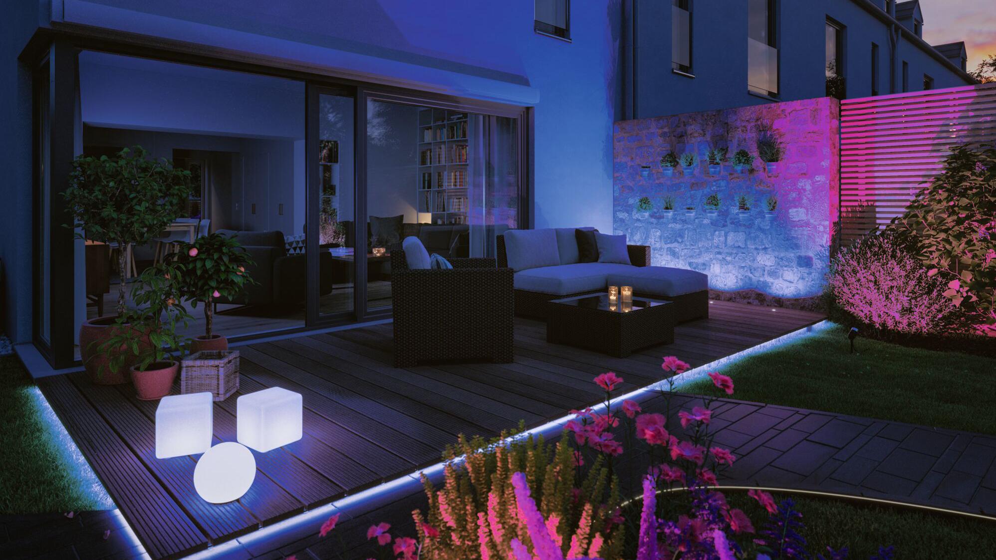 Terrasse moderne avec éclairage LED au sol et plantes colorées, mobilier lounge en rotin confortable.