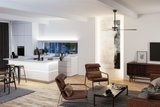 Modern living room with brown fabric armchairs, wooden coffee table, and white kitchen island with LED lighting