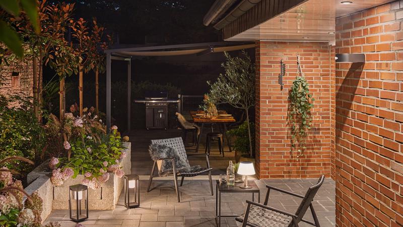Gemütliche Außenbeleuchtung mit modernen LED-Laternen und Wandlampe an roter Backsteinmauer im Garten.