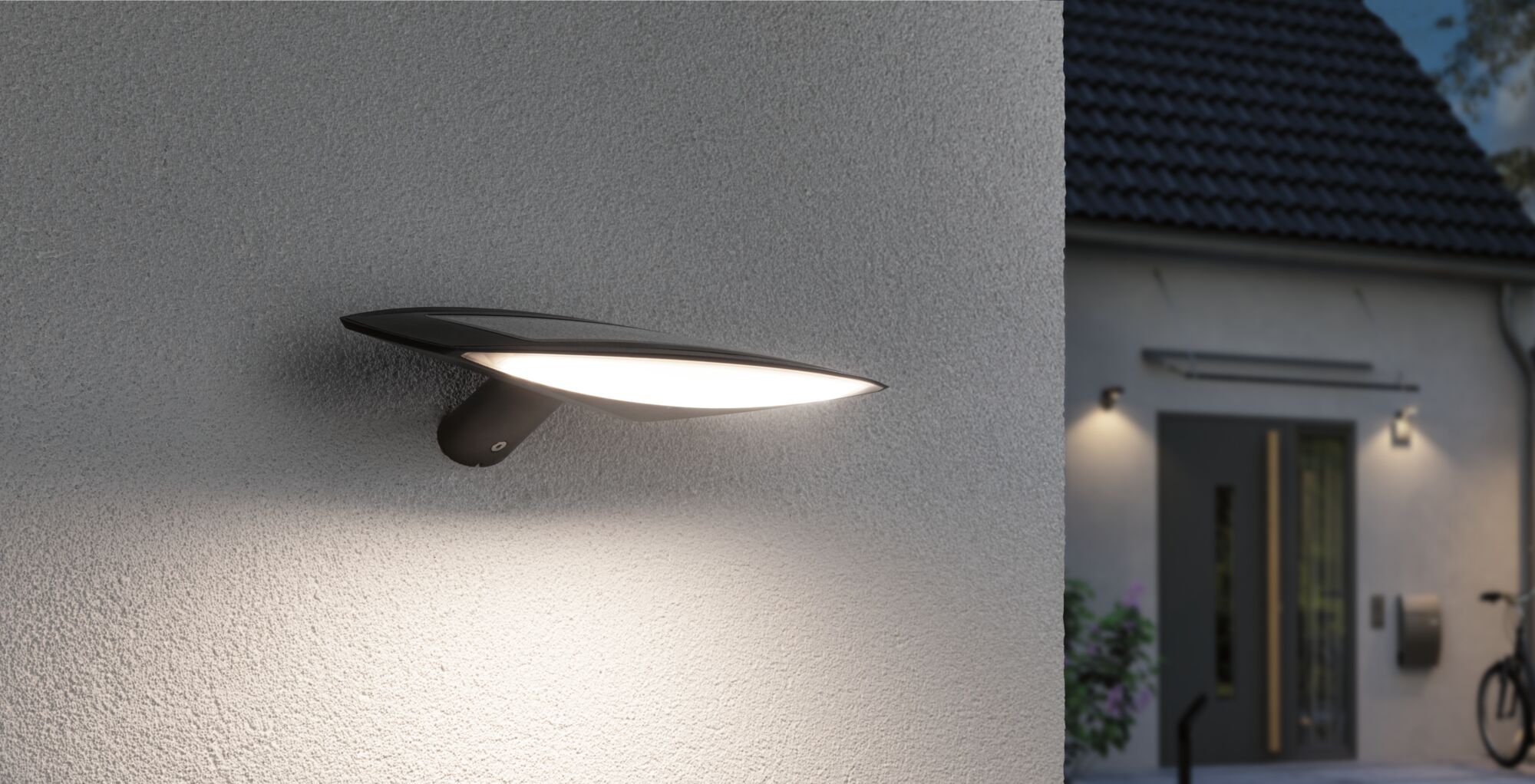 Moderne schwarze Außenwandleuchte mit breitem LED-Lichtschein an Hausfassade für Gartenbeleuchtung