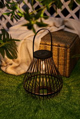 Zwarte metalen solar lantaarn met lamp op groen gras in tuin naast rieten mand en deken