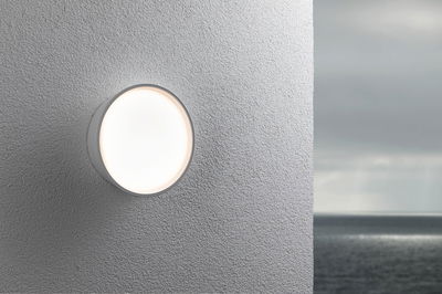 Round white outdoor wall light made of plastic on grey wall with sea background, LED lighting