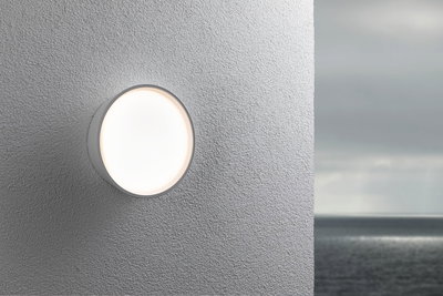 Applique murale extérieure ronde blanche en plastique sur mur gris avec vue sur mer, éclairage LED