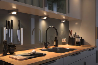 Moderne Küchenarbeitsplatte mit Holz, schwarzer Spüle, Armatur und LED-Unterbauleuchten für Küchenbeleuchtung.