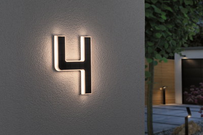 Leuchtende Hausnummer 4 aus schwarzem Material mit warmweißem LED-Licht an grauer Wand im Außenbereich