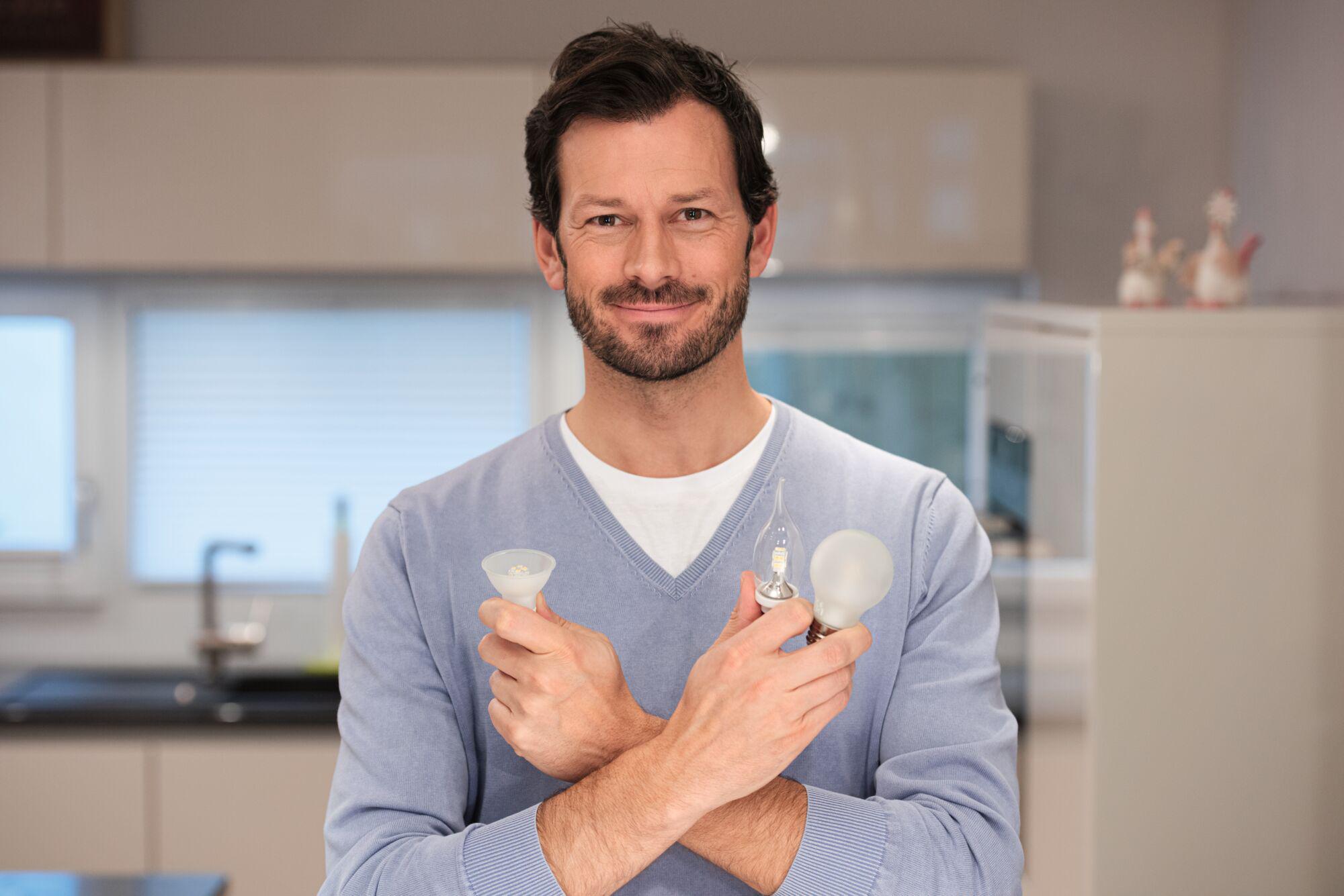 Mann hält drei verschiedene LED-Leuchtmittel in Weiß und transparent, moderne Energiesparlampen