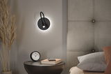 Black LED wall light with flexible arm on grey wall beside bed and nightstand with clock and book