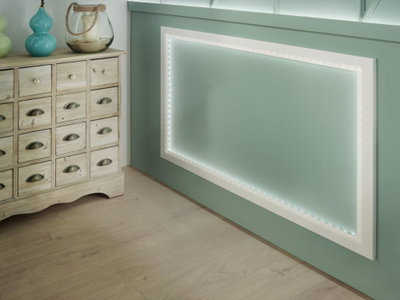 Weiße LED-Rahmenleuchte an grüner Wand mit Holzkommode und Deko im modernen Wohnraum