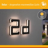 Solarhausnummer 2d aus schwarzem Material mit warmweißem Licht an grauer Wand beleuchtet