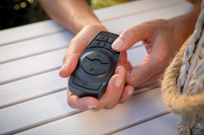 Black remote control with large buttons held in hand on white wooden table, LED lighting accessory