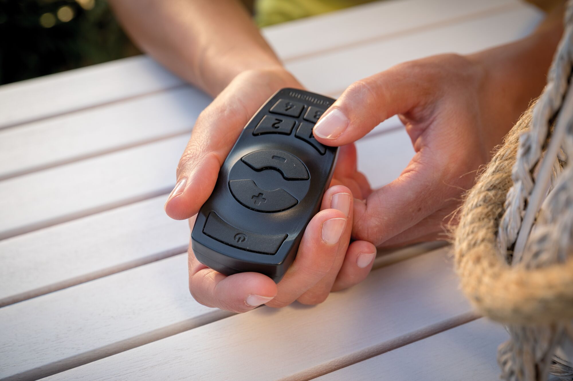 Black remote control with large buttons held in hand on white wooden table, LED lighting accessory