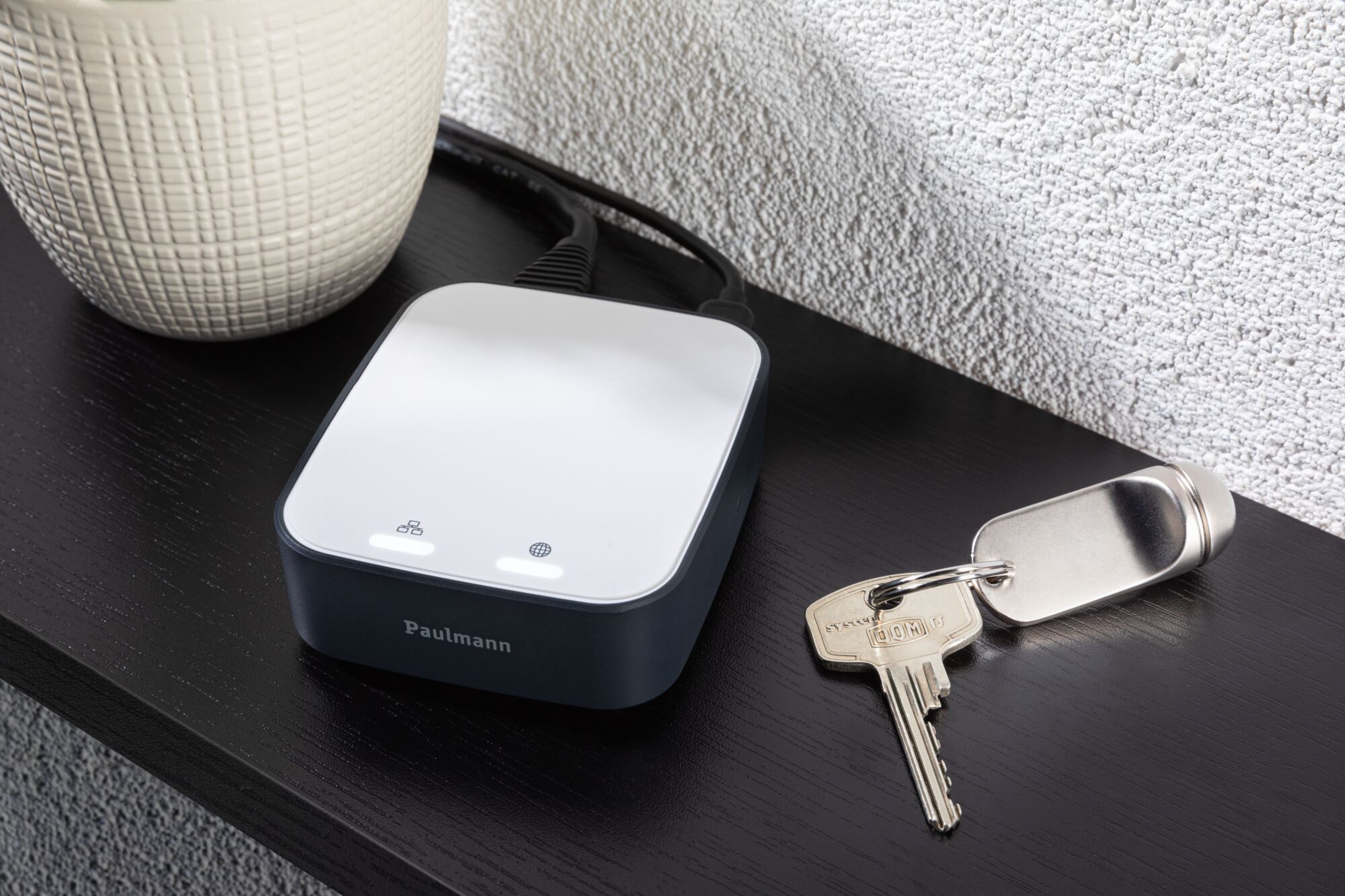 Compact Paulmann smart home gateway in black and white on black table next to keychain.