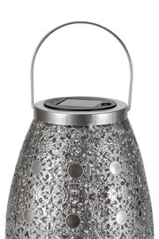 Metal lantern with intricate pattern and solar panel on top for energy-saving outdoor lighting
