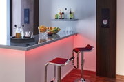 Moderner Barbereich mit roten LED-Leisten, zwei schwarzen Barhockern und Holzlautsprechern an der Wand