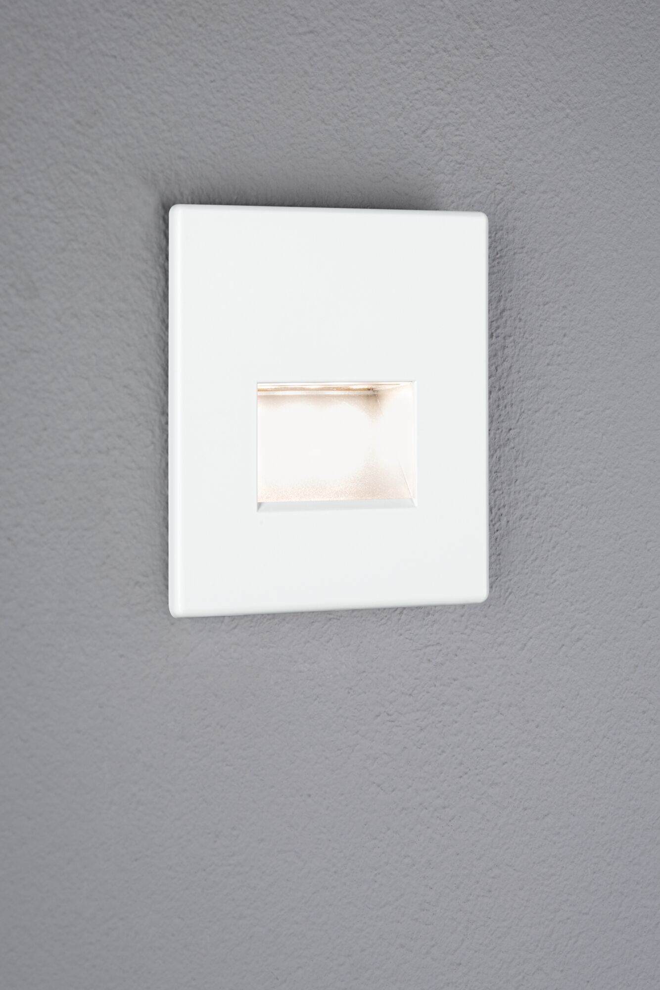 Weißer quadratischer LED-Wandeinbauleuchte mit warmweißem Licht an grauer Wand