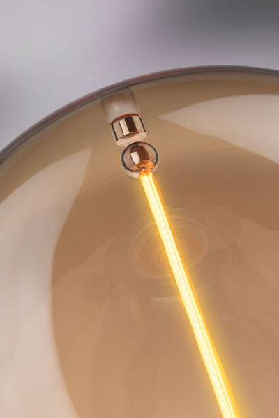 Close-up of warm glowing LED filament inside amber glass lamp shade for ambient lighting