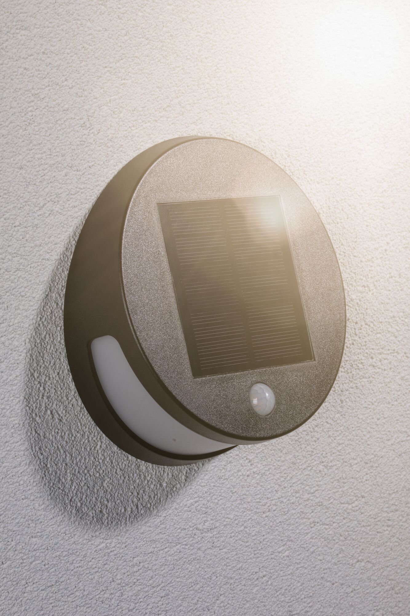 Round grey solar wall light with motion sensor on white exterior wall for energy-saving outdoor lighting