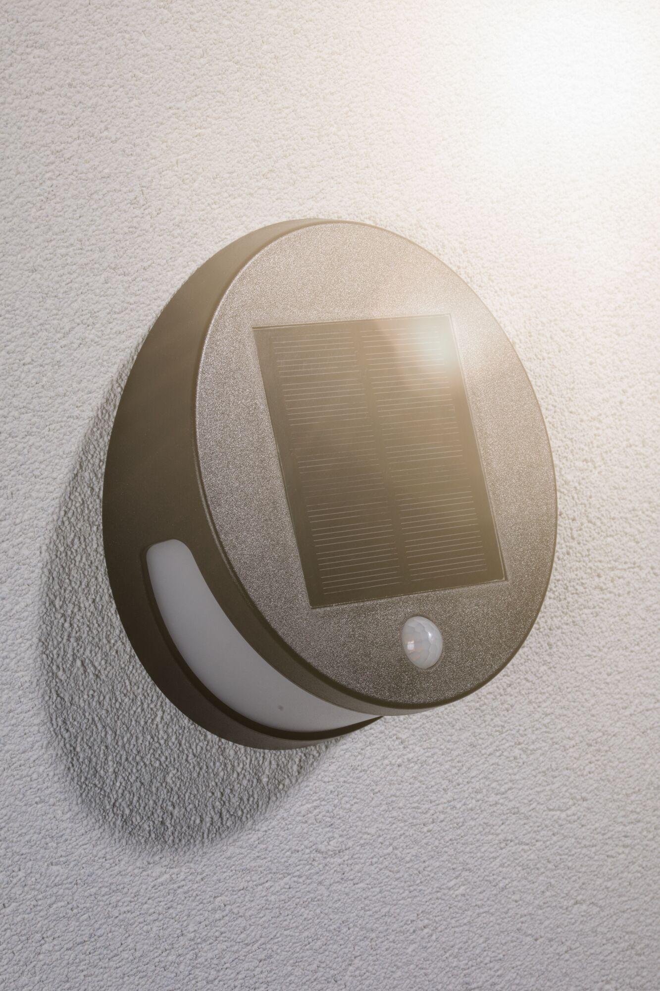 Ronde bruine solar buitenwandlamp met bewegingssensor gemonteerd op witte gestructureerde muur voor energiebesparing