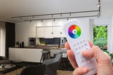 Télécommande blanche avec roue chromatique pour éclairage LED dans un salon moderne avec cuisine ouverte.
