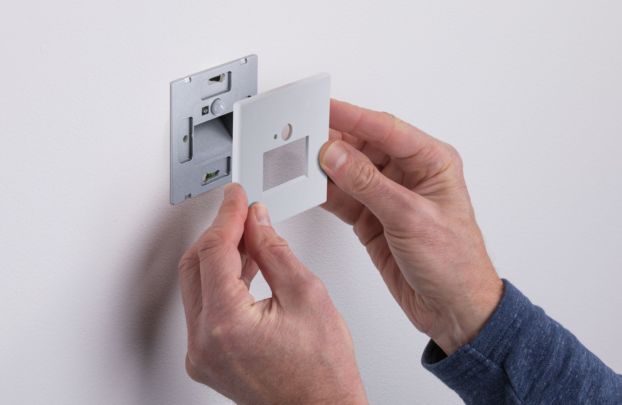 Installing white plastic cover plate on metal wall mount for light switch in home interior.