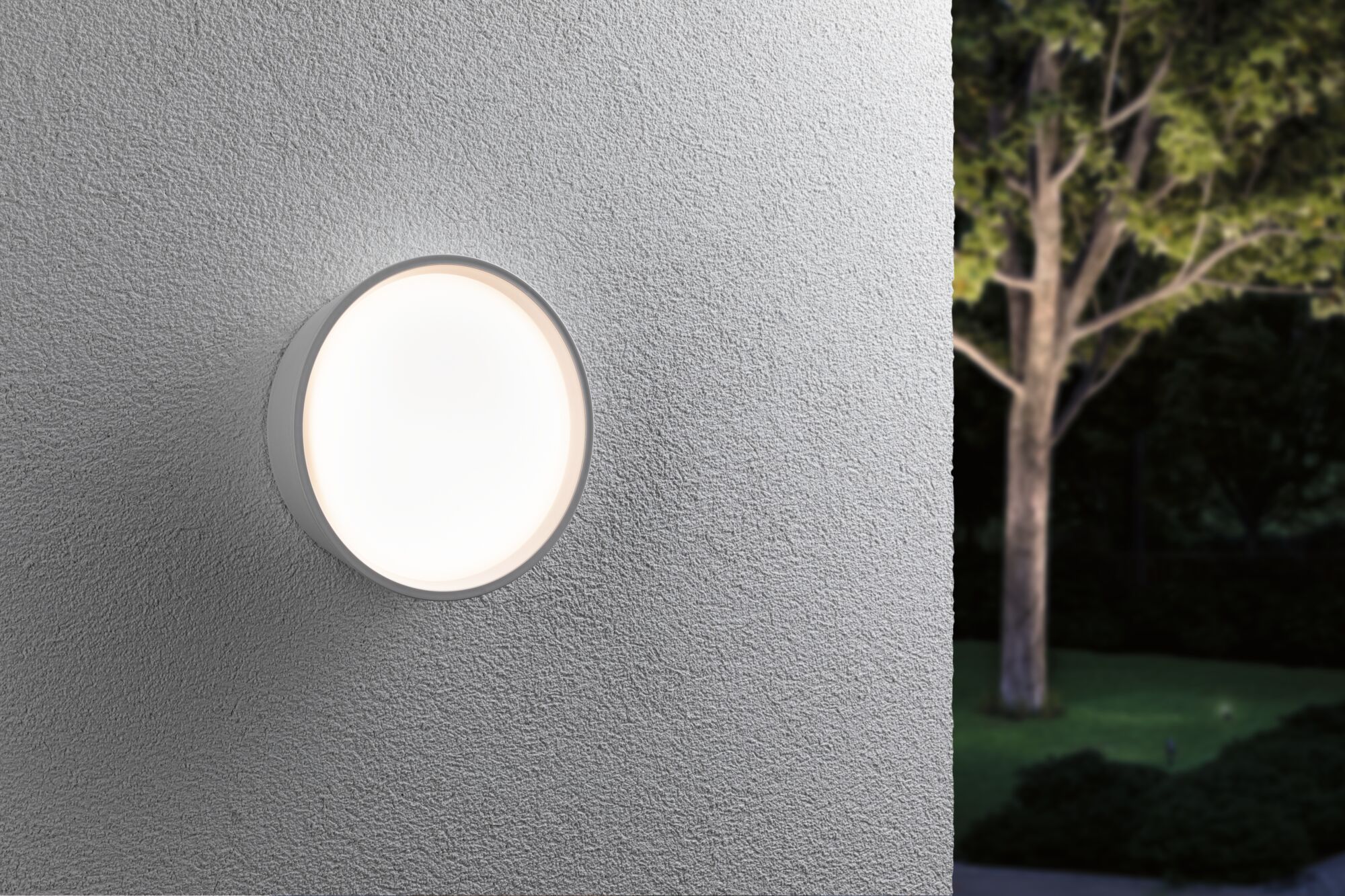 Round white LED outdoor wall light on grey wall emitting soft light for garden lighting