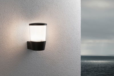 Black outdoor wall light with white glass on white wall, ambient lighting for terrace or garden