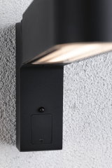 Black metal outdoor wall light with built-in sensor mounted on white textured wall for garden lighting