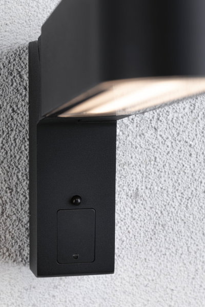 Black metal outdoor wall light with built-in sensor mounted on white textured wall for garden lighting