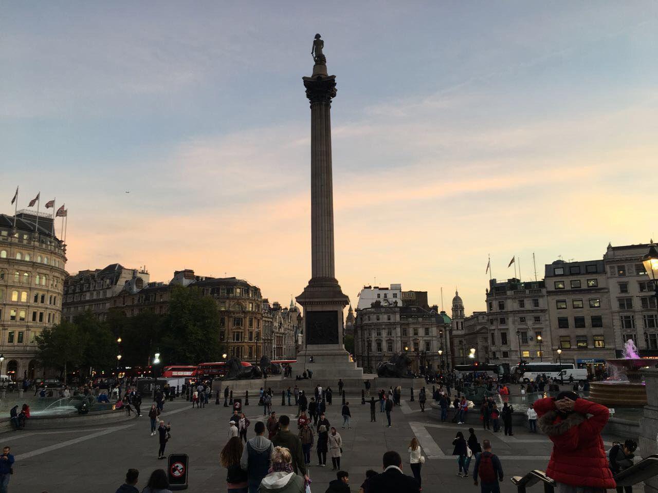 Menschen am Trafalgar Square mit Nelsonsäule und historischen Gebäuden bei Sonnenuntergang in London