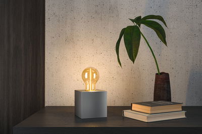 Moderne tafellamp met grijze metalen kubus en warmwitte LED-lamp op donker houten oppervlak.