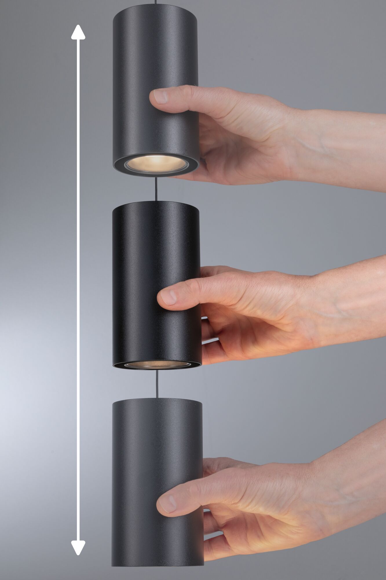 Drei schwarze zylindrische LED-Pendelleuchten aus Metall, die von Händen gehalten werden, mit Höhenverstellfunktion.