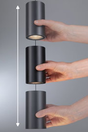 Drei schwarze zylindrische LED-Pendelleuchten aus Metall, die von Händen gehalten werden, mit Höhenverstellfunktion.