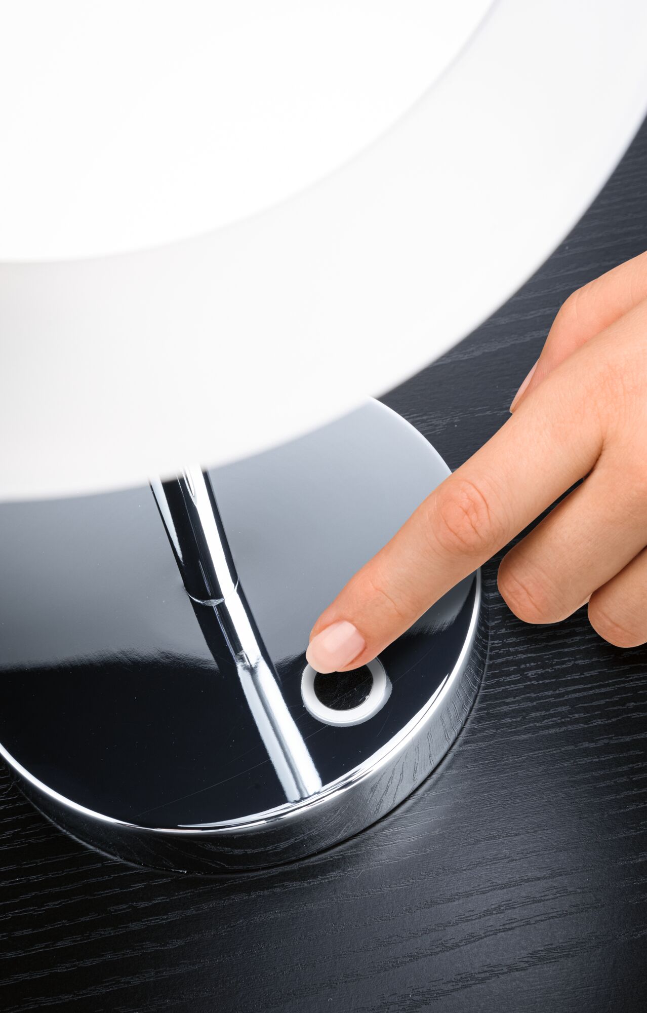 Hand tippt auf runden Touch-Schalter einer chromfarbenen LED-Tischlampe auf schwarzem Holztisch