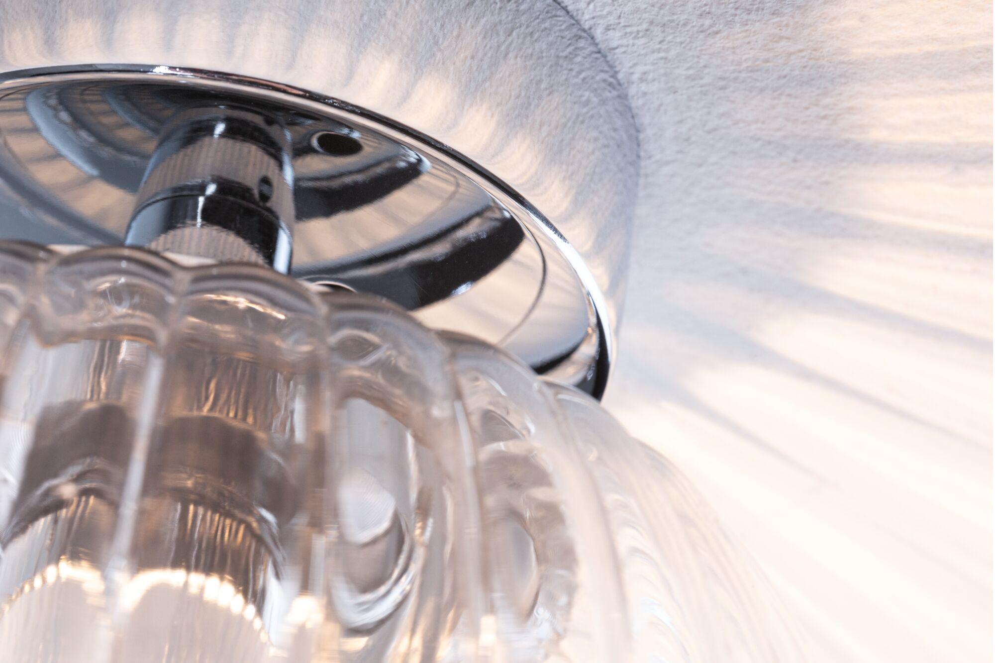 Close-up of transparent glass lamp with chrome mount on white ceiling, LED lighting effect