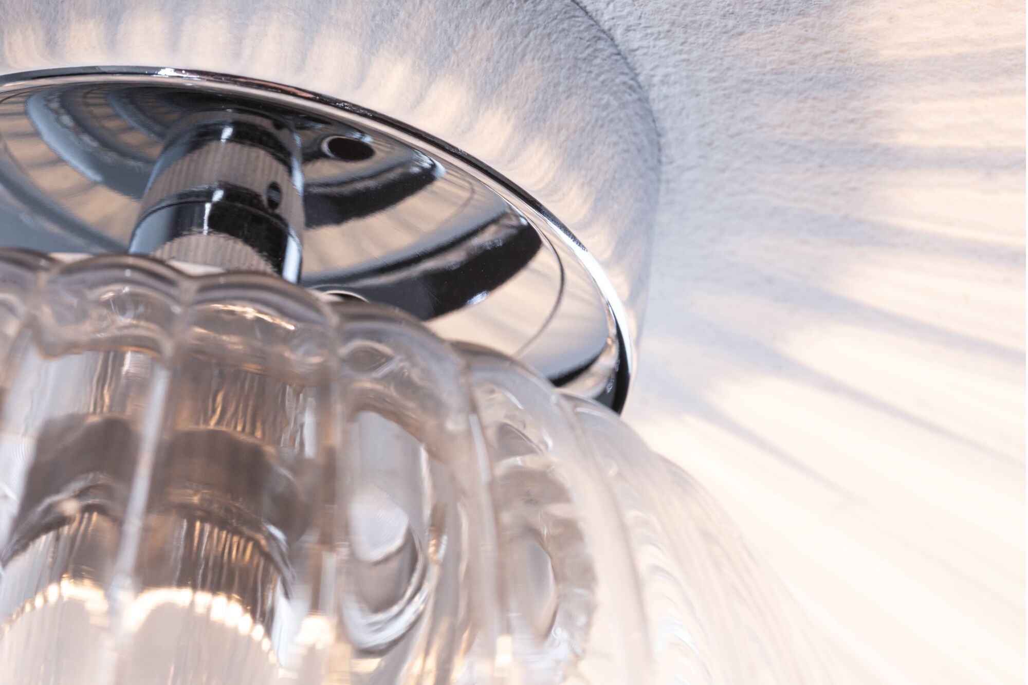 Gros plan d'un plafonnier en verre transparent avec support chromé et reflets lumineux