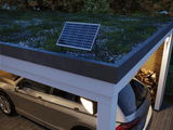 Zonne-energie buitenlamp met zwart frame op moderne carporthoek met groen dak en geparkeerde auto.