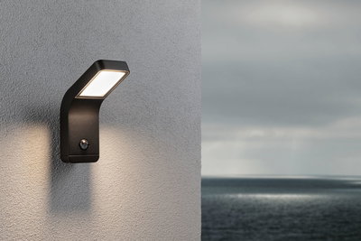 Black metal LED outdoor wall light with motion sensor mounted on grey wall by the sea