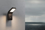 Black metal LED outdoor wall light with motion sensor mounted on grey wall at dusk