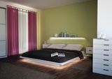 Modernes Schlafzimmer mit beleuchtetem weißen Bett, grünem Wandregal und pinken Vorhängen für gemütliche Atmosphäre
