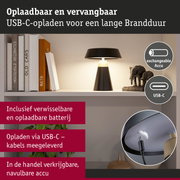 Zwarte tafellamp met USB-C oplaadkabel en verwisselbare accu op witte plank met boeken