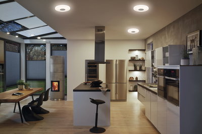 Moderne Küche mit weißen Hochglanzfronten, Holzarbeitsplatte und runden Deckenleuchten in warmweißem Licht.