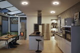Moderne Küche mit weißen Hochglanzfronten, Holzarbeitsplatte und runden Deckenleuchten in warmweißem Licht.
