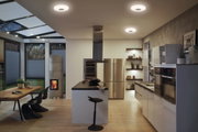 Moderne Küche mit weißen Hochglanzfronten, Holzarbeitsplatte und runden Deckenleuchten in warmweißem Licht.