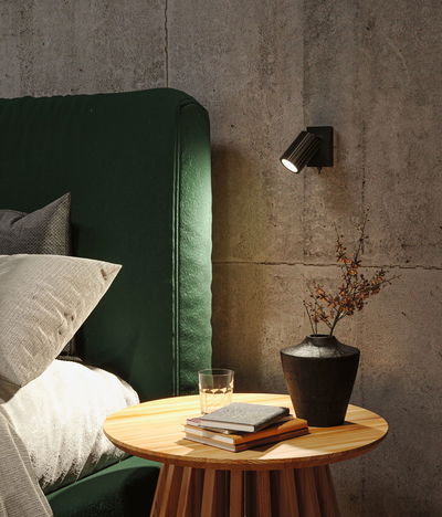 Black metal LED wall light on concrete wall above wooden table with vase and books in bedroom