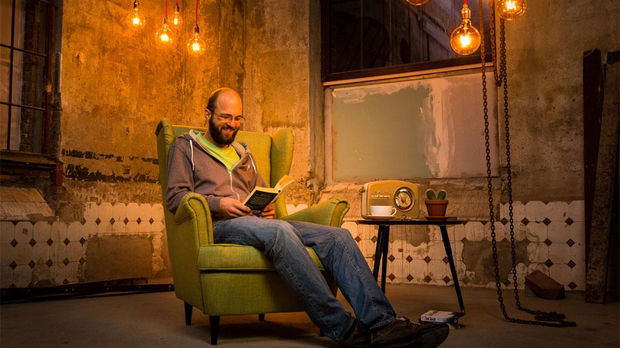 Man reading book in green armchair under warm filament bulb lighting in rustic room setting