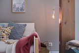 Weiße Holzbank mit bunten Kissen und Wandlampe mit sichtbarer Glühbirne an Holzbalken im Wohnzimmer