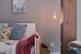 White wooden bench with colorful cushions and wall lamp with visible bulb on wooden beam in living room