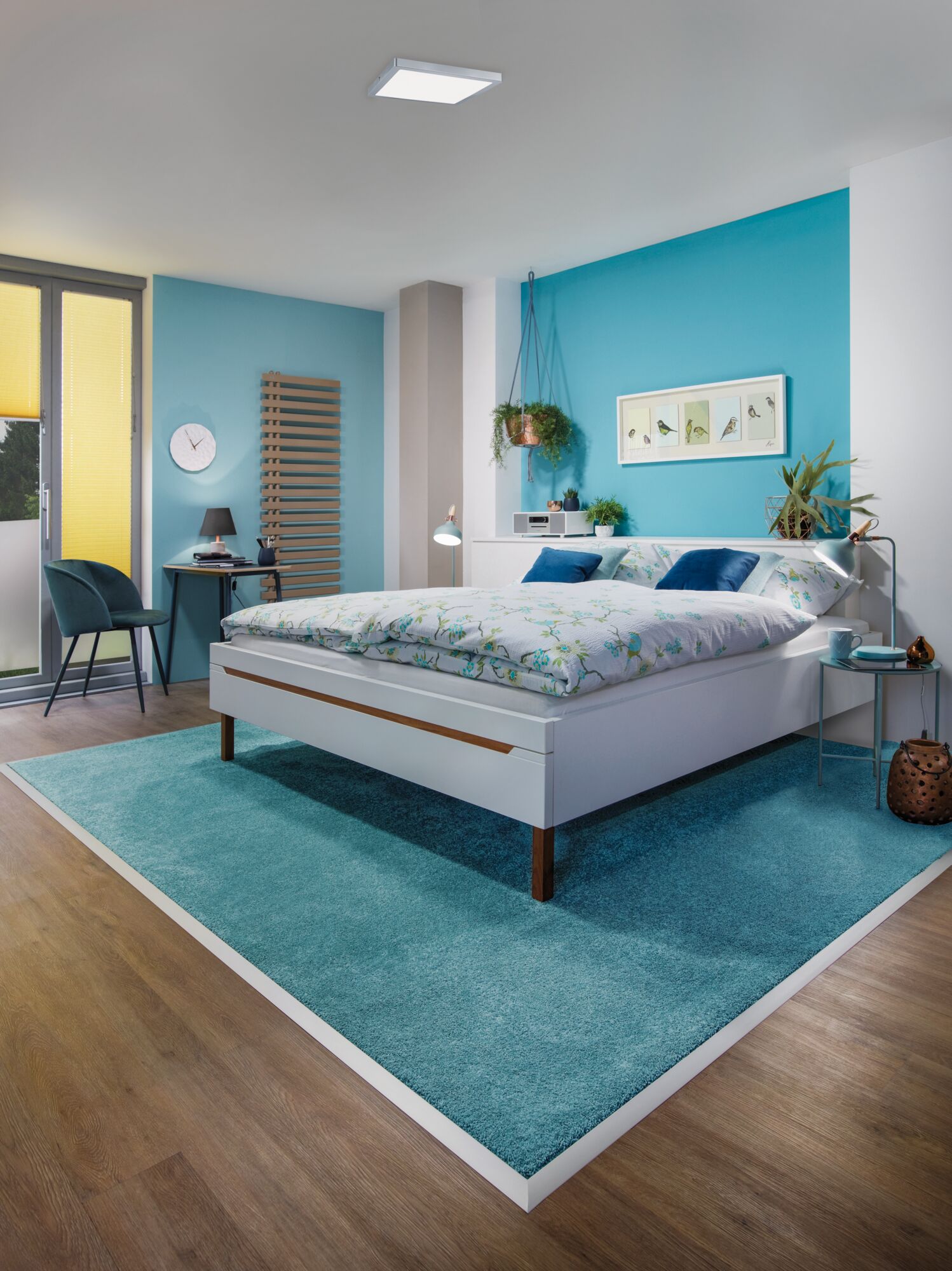 Modern bedroom with white bed, blue rug, and turquoise wall creating a cozy interior design